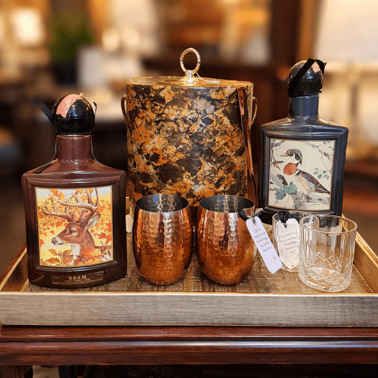 Curated vintage barware display at Reclaimed Rose featuring collectible bourbon bottles, hammered metal cups, glassware and vintage accessories.